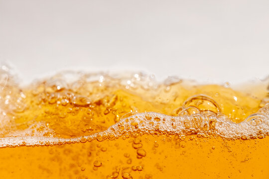 Close up of golden beer splashing with bubbles and foam in a glass, creating dynamic liquid movement. Refreshing alcoholic drink background for commercial beverage advertising and design