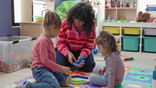 Teacher kneels and hands a blue block to two girls on a colorful foam playmat in building; focused play learning.