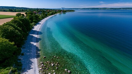 Obraz premium Luftaufnahme einer langen Küstenlinie mit türkisblauem Wasser, weißen Kieselsteinen und einem Stadtbild in der Ferne.