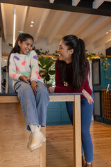 Indian mother and daughter sitting on kitchen island chatting, child holding phone © wavebreak3
