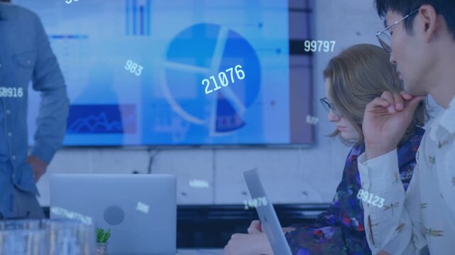Team lead moving in gesturing at screen, numbers showing data charts while team typing laptops