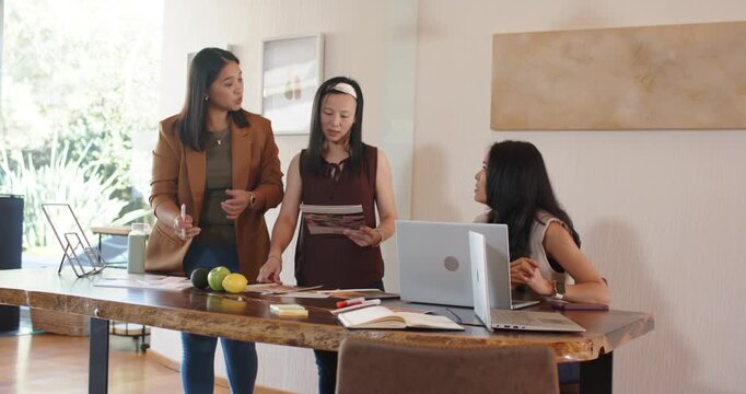 Diverse women planning at home seated starting talking center holding brochure left sorting samples