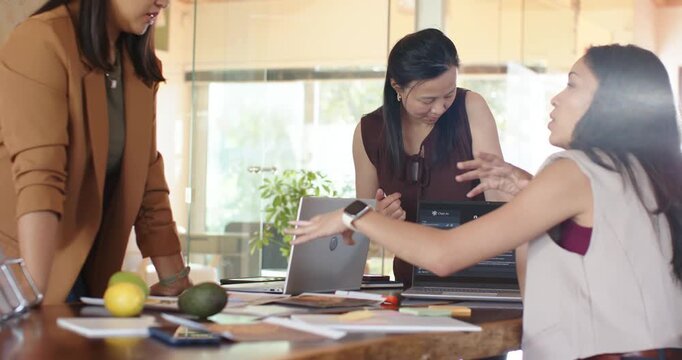 Diverse female team discussing, deciding plan after reviewing docs and passing card at wooden table