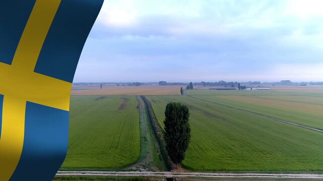 Waving Swedish flag overlaying left edge starting aerial pull moving to lone tree showing farmland