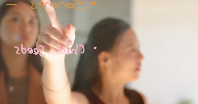 Diverse women pointing at Chia Seeds on glass panel, tracing list with markers, planning food