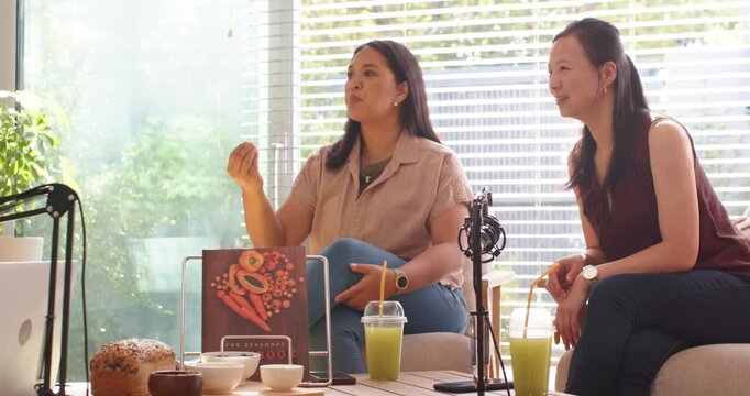 Diverse women speaking, gesturing as tablet guest enters, discussing cookbook in studio near mics
