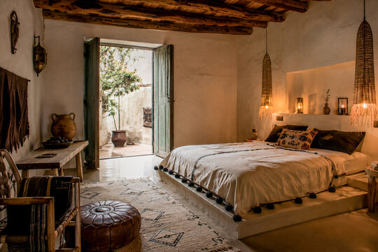  Apartamento real r&uacute;stico con cama blanca, vigas de madera y puerta abierta hacia un patio soleado mediterr&aacute;neo. El espacio transmite calma y autenticidad artesanal.