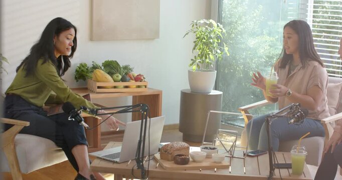 African American women recording podcast, left host moving mic, using laptop and offering smoothie