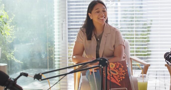 Female hosts recording in studio, Asian host reacting to left host remark, laughing into boom mic