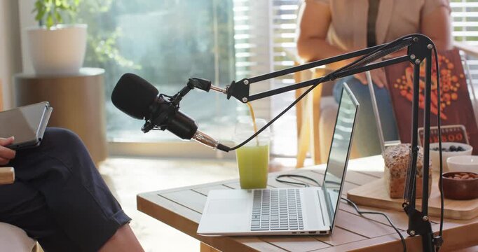Diverse female hosts tuning mic boom as second boom entering, prepping laptop, tablet for recording