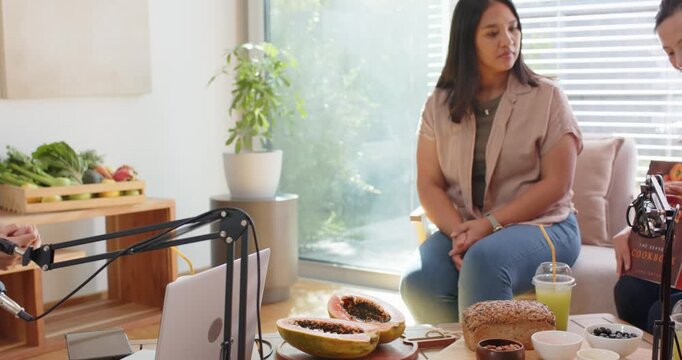 Diverse female hosts speaking on mic in studio, Asian host arranging papaya bread drink for show