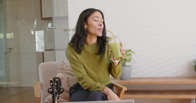 Woman seeing jar reaching raising green drink sipping straw reacting offscreen with laptop mic