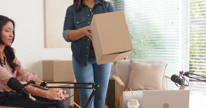 Female colleagues watching while woman in denim carrying box for product demo near microphones