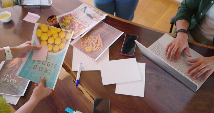 Diverse coworkers starting layout review at studio table, arranging VEGGIE BOWL SALADS BREAD covers