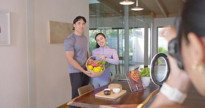 Couple posing at table, holding fruit basket, showing menu while shooter placing camera, ringlight