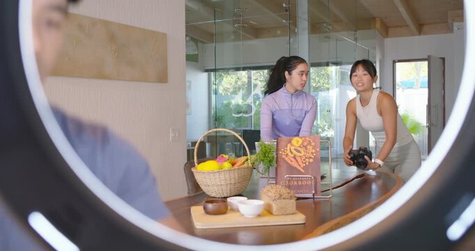 Diverse team high-fiving placing cookbook and basket at table framing DSLR under ring light for ads
