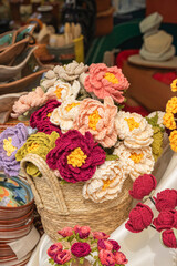 Crochet flower bouquet fills woven basket at craft stall, with handmade yarn roses and blossoms...