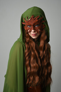 fantasy close up portrait of beautiful female model wearing leaf mask and green hooded cloak,  historical pagan fae  halloween costume. isolated figure on studio background.