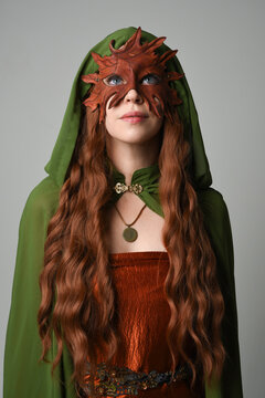 fantasy close up portrait of beautiful female model wearing leaf mask and green hooded cloak,  historical pagan fae  halloween costume. isolated figure on studio background.