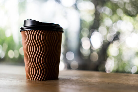 Brown paper coffee cup with black lid on table against nature background
