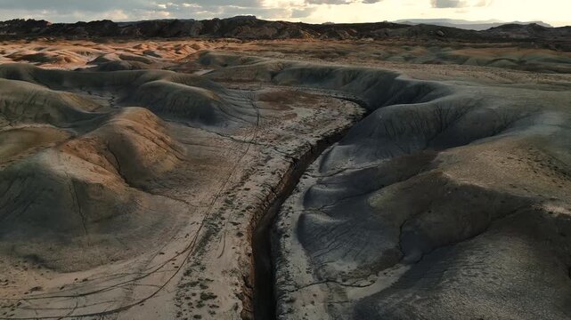 16 March 2026: Aerial view of a deep crevice winding through desert badlands under a dramatic sunset sky with rolling hills and golden light.