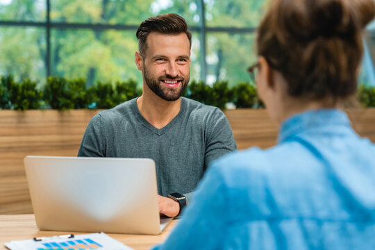 Male worker and customer having a discussion at the office desk while using a laptop, collaborating on tasks and sharing information in a professional setting.