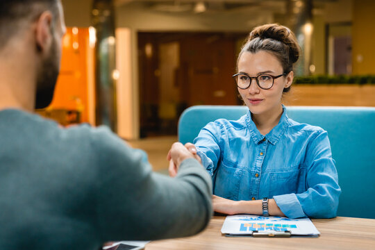 Two young business partners shaking hands in a modern office, finalizing a deal with confidence and professionalism in a sleek and dynamic work environment.
