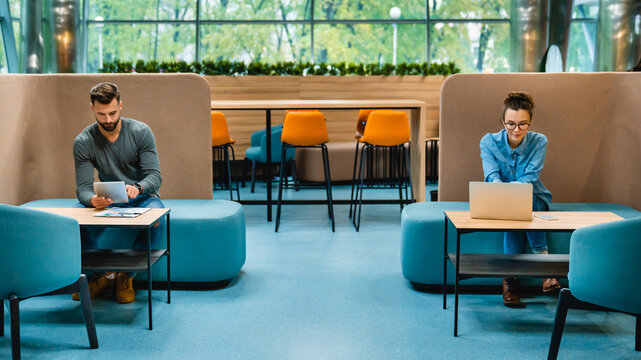 Social distancing concept: Two colleagues sitting 1.5 meters apart, wearing medical masks in a modern office. Horizontal shot highlighting safety measures in a professional workspace.