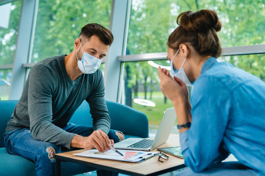 Two Caucasian business partners wearing medical masks, signing a contract in the office, ensuring safety while finalizing a professional agreement in a modern workspace.