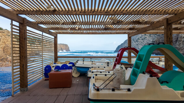 View of Spiaggia di Cala Domestica with pedal boats stored under a wooden pergola overlooking the sea and rocky cliffs in Provincia del Sulcis Iglesiente, Sardegna, Italy.