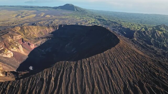 Ambrym Island volcanic caldera with massive Mount Benbow crater, rugged ash covered terrain and contrasting distant green vegetation in Vanuatu's dramatic volcanic landscape. Aerial drone panorama