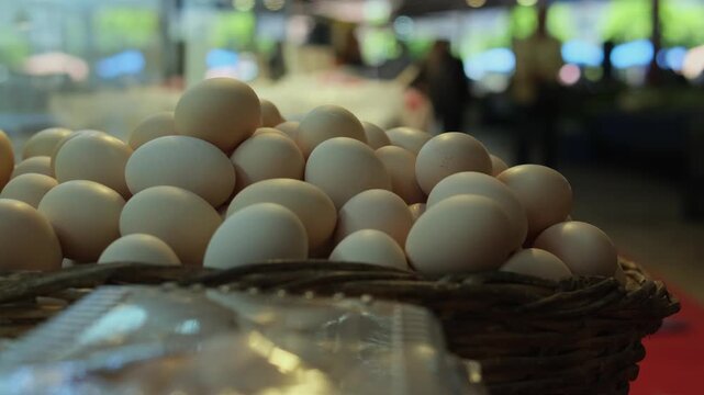Basket of farm eggs piled on market stall, warm brown shells and wicker texture, blurred shoppers in background, wholesome pasture to table feel, organic