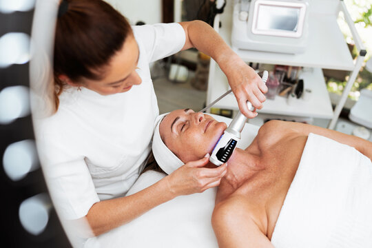 A professional aesthetician uses advanced beauty roller technology for skin tightening and body contouring on a relaxed client in a spa salon.