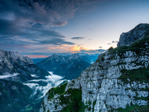 Alpine landscape featuring rugged mountain peaks and valley mist at sunset, ideal for nature tourism and exploration, Mangart, Julian Alps, Italy-Slovenia border.