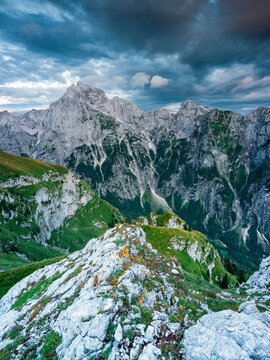 Alpine mountain peaks rise above lush green slopes, offering a dramatic travel destination for outdoor nature adventure and tourism in the rugged Mangart, Julian Alps, Italy-Slovenia border.