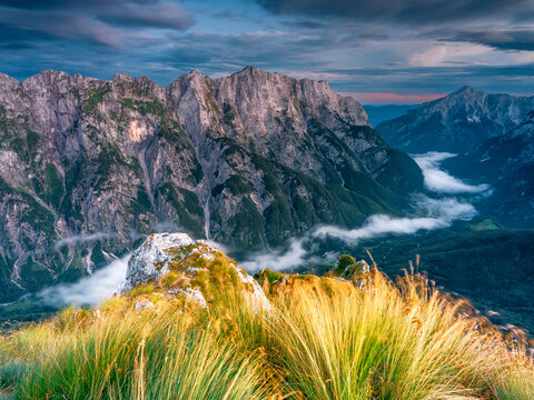 Alpine mountain peaks rise above a fog-filled valley, offering a sense of rugged exploration and tourism in this nature landscape at Mangart, Julian Alps, Italy-Slovenia border.