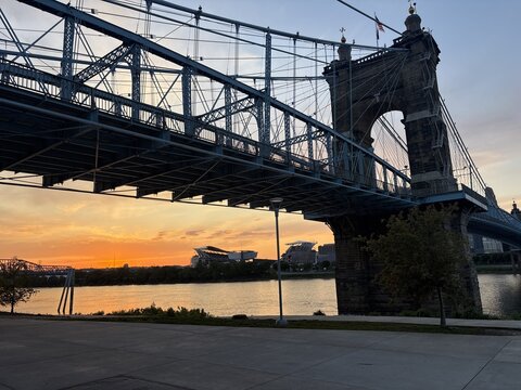 View of the John A. Roebling Suspension Bridge spanning the Ohio River at sunset with a stadium in the background Covington, Kentucky, United States.