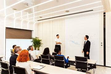 Professionals attend a business presentation in a modern boardroom while two presenters explain...