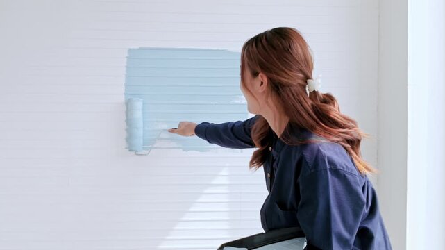 Person using a paint roller to apply light blue paint on a white paneled interior wall during a DIY home renovation.