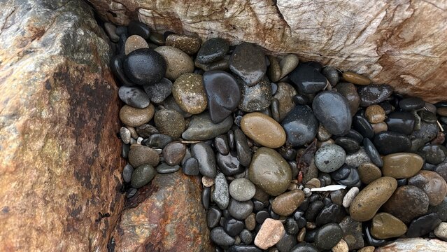 View of smooth wet pebbles and river stones nestled between large textured rocks Oceanside, California, United States.