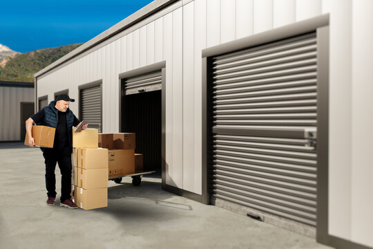 Self storage facility. Man unloads cardboard boxes from storage unit and checks inventory on tablet during moving service