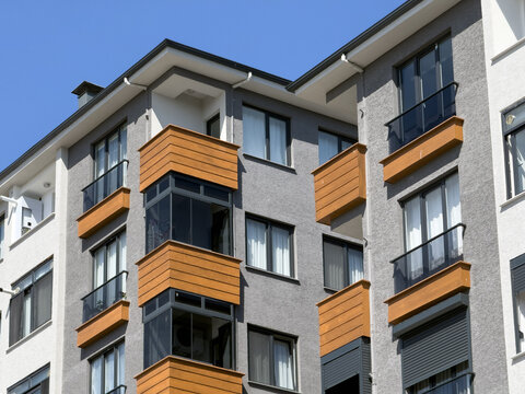 View of modern residential building facade with grey walls and orange balcony accents under a clear blue sky in Avcilar, Istanbul, Turkiye.