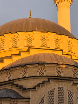 View of the golden domes and minaret of a mosque during sunset with intricate window details in Avcilar, Istanbul, Turkey.