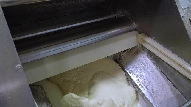 Close-up of an automated dough sheeter in a bakery processing raw dough. The professional equipment is laminating and kneading the mass for making bread