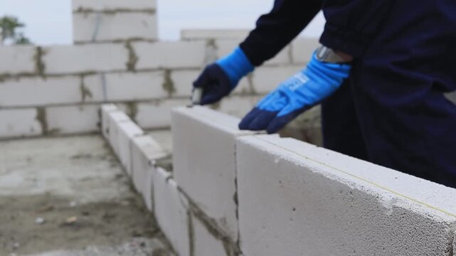 Worker laying aerated concrete blocks at a construction site, soft focus shot with no focus on the main subject.