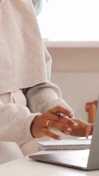 Faceless Woman Writing in Notebook and Typing on Laptop in Minimalist White Workspace