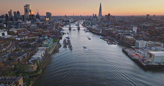Aerial view of London skyline at dusk with the River Thames, Tower Bridge and The Shard framed by boats and evening light, blending historic landmarks and modern skyscrapers. Drone shot panorama