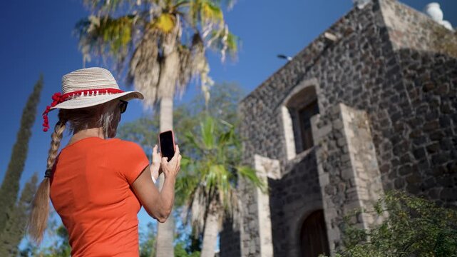 Mature woman enjoys her adventure discovering the Mission Church Santa Rosalia in Mulege with lush palm trees and desert mountains.