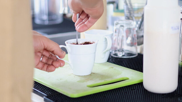 Person Stirring Cocoa Powder into a White Cup on a Green Board