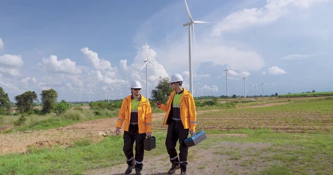 caucasian engineer in safety uniform holding toolbox looking at wind turbines, renewable power project concept, teamwork for clean energy, professional outdoor maintenance under bright cloudy sky